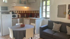 A compact kitchen with a dining table, white chairs, a gray sofa, and a window with a view of greenery. - Holiday Home in Lacoste with Pool (Lacoste)