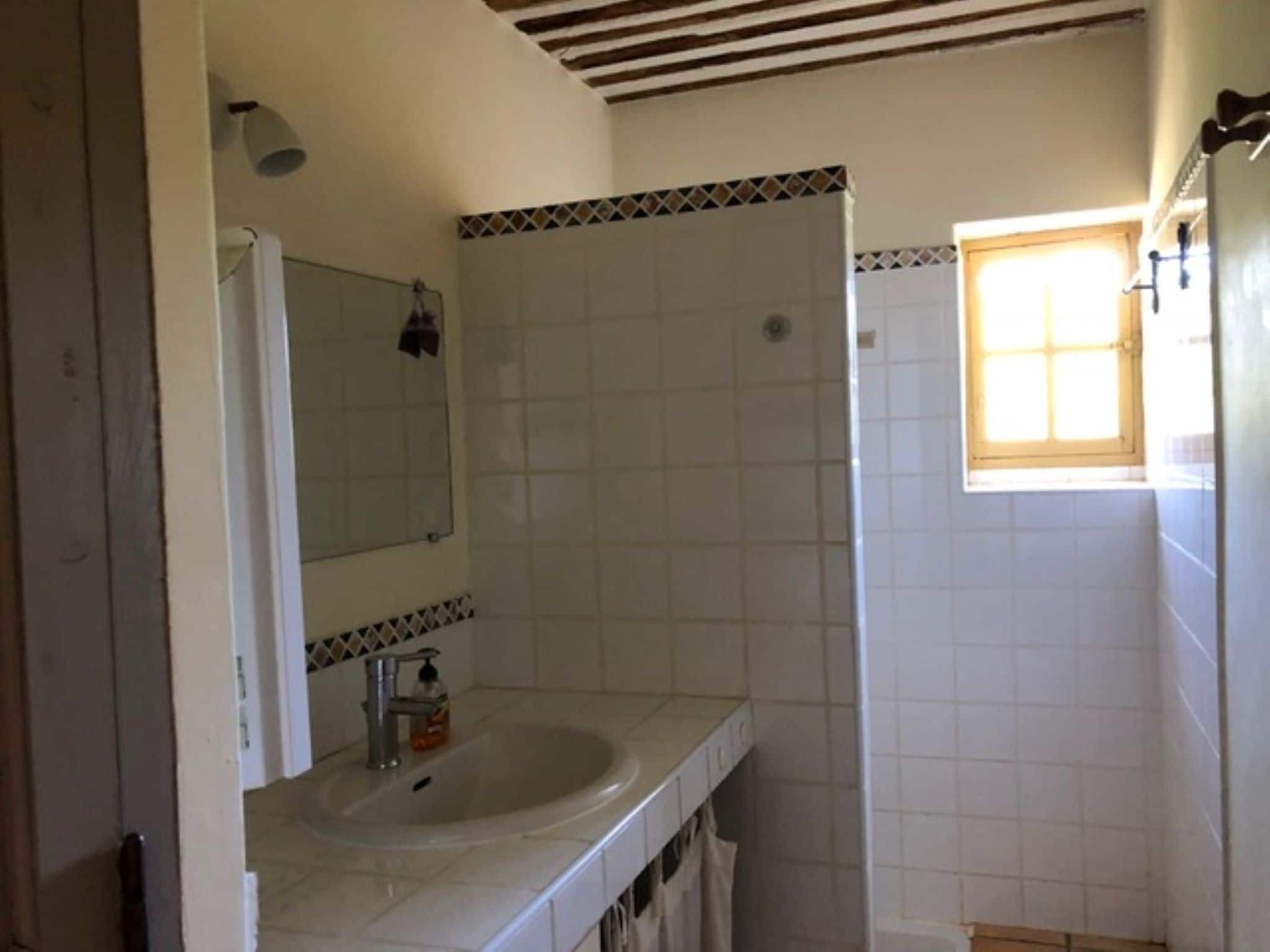 Un baño con lavamanos, espejo y una ventana pequeña.