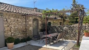 A stone building with a tiled roof, a covered patio with a table and chairs, and a gravel area. - Holiday Home in Lacoste with Pool (Lacoste)