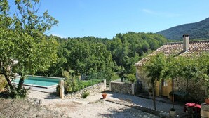 A courtyard with a swimming pool, stone walls, and a view of a forested hill. - Holiday Home in Lacoste with Pool (Lacoste)