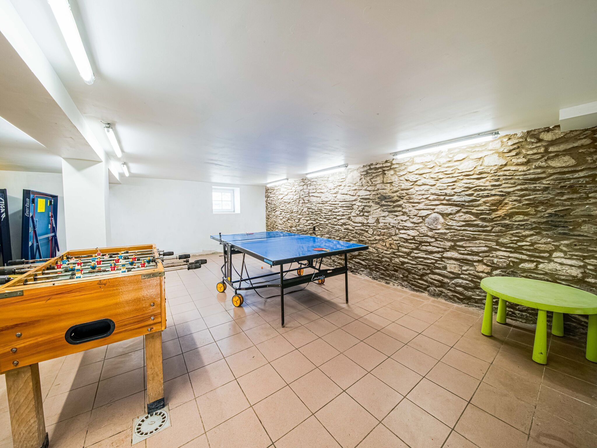 A room with a foosball table, ping pong table, and a stone wall.
