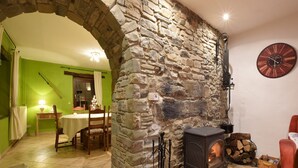 Une pièce chaleureuse avec un mur en pierre, une cheminée, un coin repas et une horloge au mur.