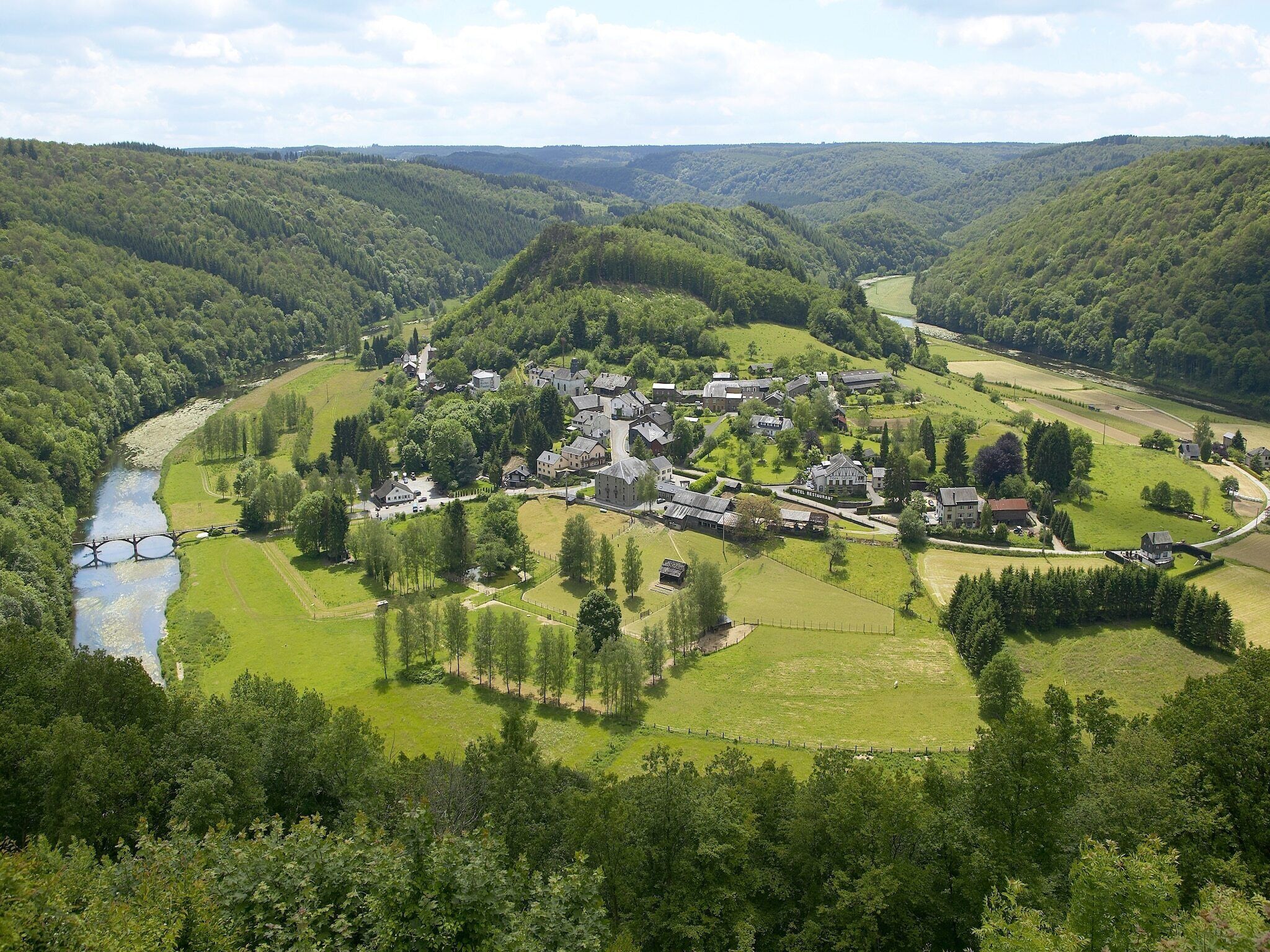 A rural village with a river, surrounded by forested hills.