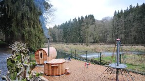 Un área boscosa con construcciones de madera, incluyendo una sauna y un espacio de juegos con un columpio.