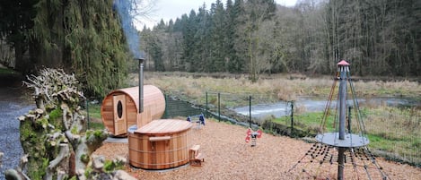 Un área boscosa con construcciones de madera, incluyendo una sauna y un espacio de juegos con un columpio.