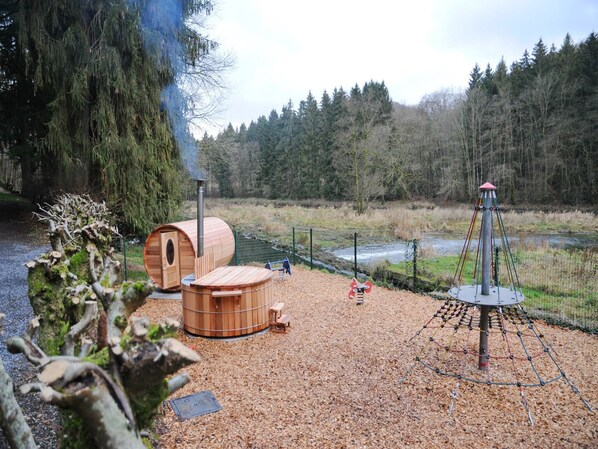 A forested area with wooden structures, including a sauna and a play area with a swing set.