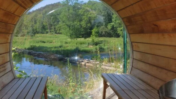 Una cabaña de madera con un ventanal circular que da a un río y un bosque.