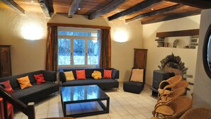 Una sala de estar acogedora con un conjunto de sofás, una mesa de centro, sillas de mimbre, una chimenea y un ventanal con cortinas.