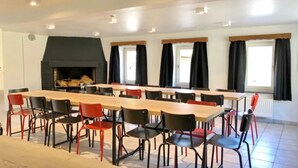 Un amplio comedor con mesas y sillas largas, una chimenea y ventanas grandes con cortinas.