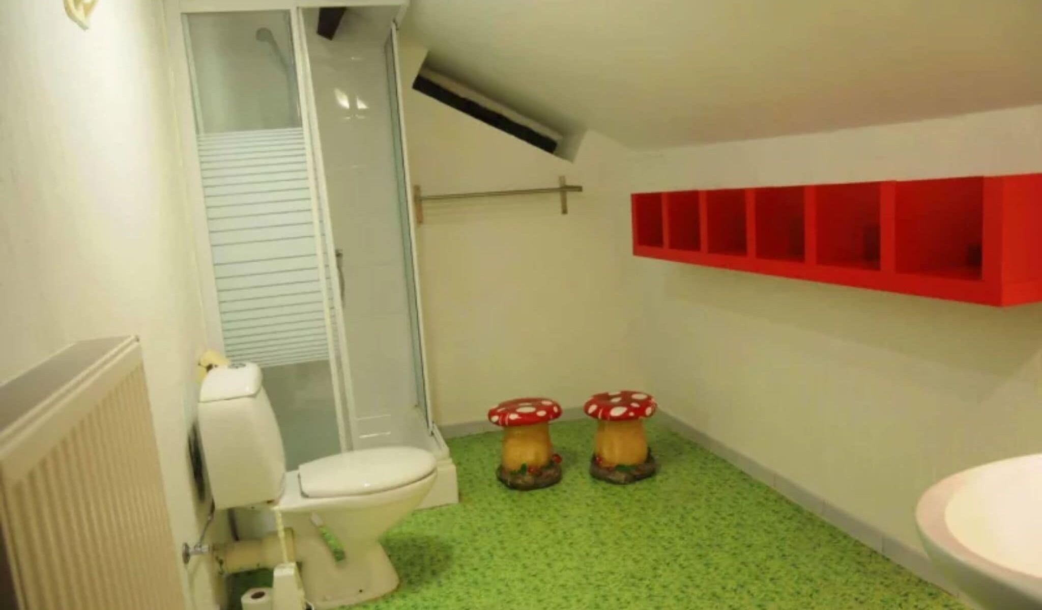 A bathroom with a toilet, shower, and a red shelf unit.