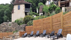 A pool area with lounge chairs and a stone wall. - Charming 1930s Home in Altillac (Altillac)