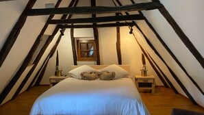 A bedroom with a large bed, wooden beams, a window, and bedside tables with lamps. - Charming 1930s Home in Altillac (Altillac)