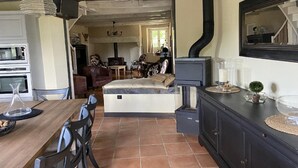 A compact living space with a dining area, a sofa, a fireplace, and a kitchen area. - Charming 1930s Home in Altillac (Altillac)