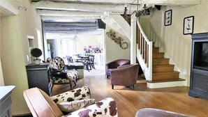 A spacious living room with a wooden staircase, a dining area, and a kitchen visible in the background. - Charming 1930s Home in Altillac (Altillac)