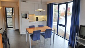 A modern kitchen with white cabinets, a dining table with blue chairs, and a large window with blue curtains. - Villa Apartment with Terrace (Durbuy)