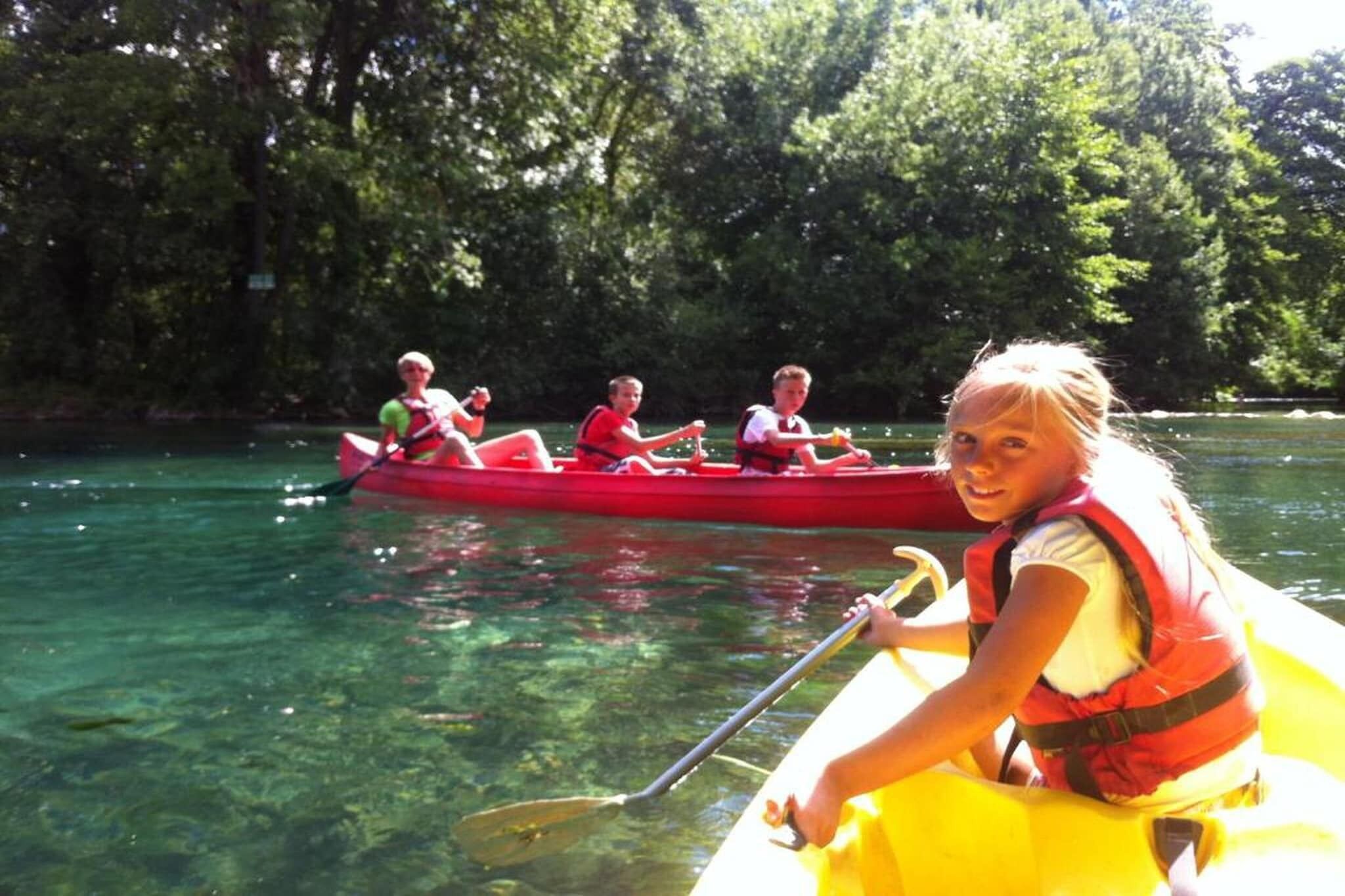 A group of people in a red canoe on a clear river surrounded by trees.