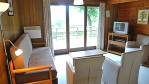 A cozy cabin interior with a sofa, chairs, a small table, a television, and a window with a view of the outdoors.