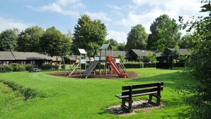 A playground with a slide and climbing structures, surrounded by a grassy area and benches.
