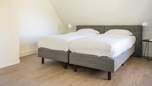 A twin bed with a grey headboard in a room with wooden flooring and white walls. - Apartment in De Cocksdorp near Beach (De Cocksdorp Texel)
