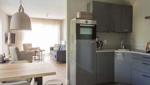 A modern kitchen with a Bosch refrigerator, a coffee maker, and a sink. There is a dining area with a table and chairs. - Apartment in De Cocksdorp near Beach (De Cocksdorp Texel)
