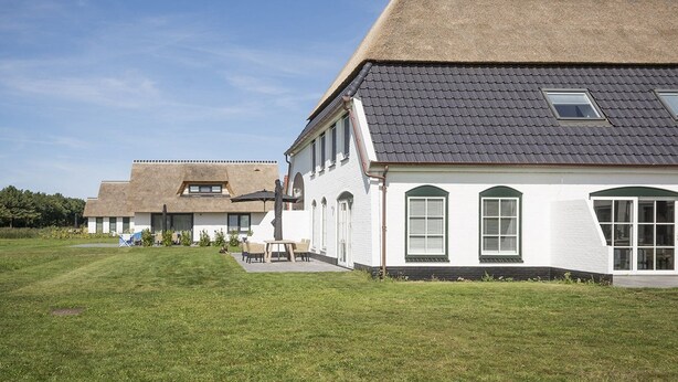 A row of white houses with grey roofs, a grassy lawn, and a clear blue sky. - Apartment in De Cocksdorp near Beach (De Cocksdorp Texel)