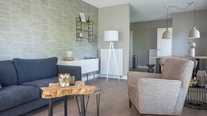 A modern living room with a grey sofa, a wooden coffee table, and a grey armchair. - Apartment in De Cocksdorp near Beach (De Cocksdorp Texel)
