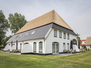 A white building with a sloped roof, large windows, and outdoor seating. - Apartment in De Cocksdorp near Beach (De Cocksdorp Texel)
