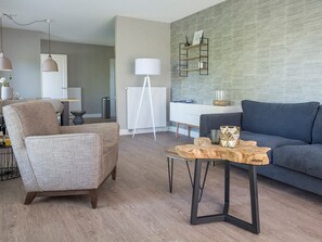 A modern living room with a grey sofa, a wooden coffee table, a grey armchair, and a white desk with a standing lamp. - Apartment in De Cocksdorp near Beach (De Cocksdorp Texel)