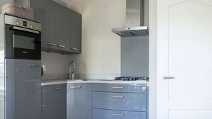 A compact kitchen with grey cabinets, a Bosch oven, a stainless steel range hood, and a white door. - Apartment in De Cocksdorp near Beach (De Cocksdorp Texel)