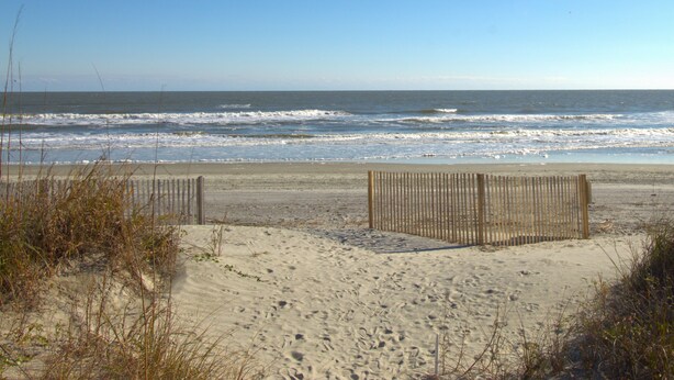 A sandy beach with a wooden fence and waves in the background.