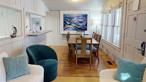 A dining area with a wooden table and chairs, a painting on the wall, and a white door with a sign.