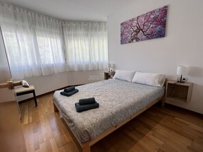 Un dormitorio con cama, una silla, una mesita de noche, una lámpara y un cuadro en la pared.