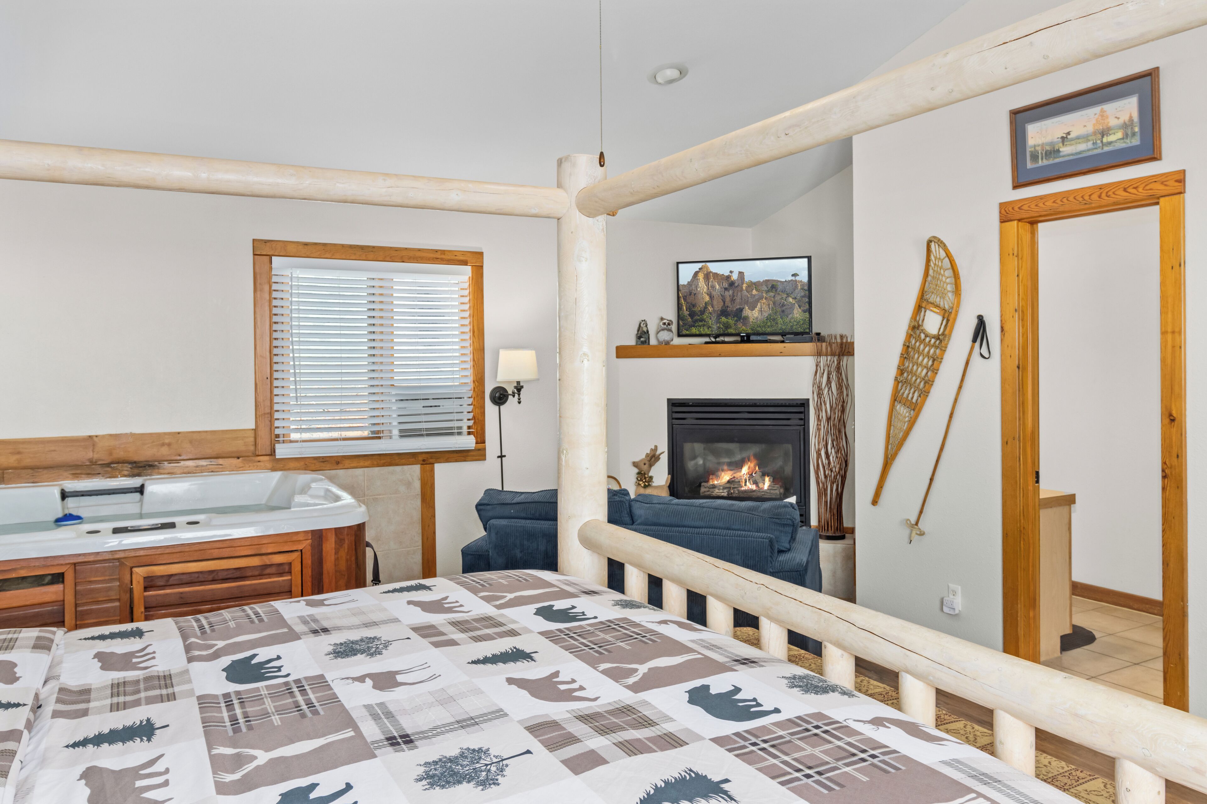 A cozy room with a bed, a fireplace, a television, and a window with blinds.