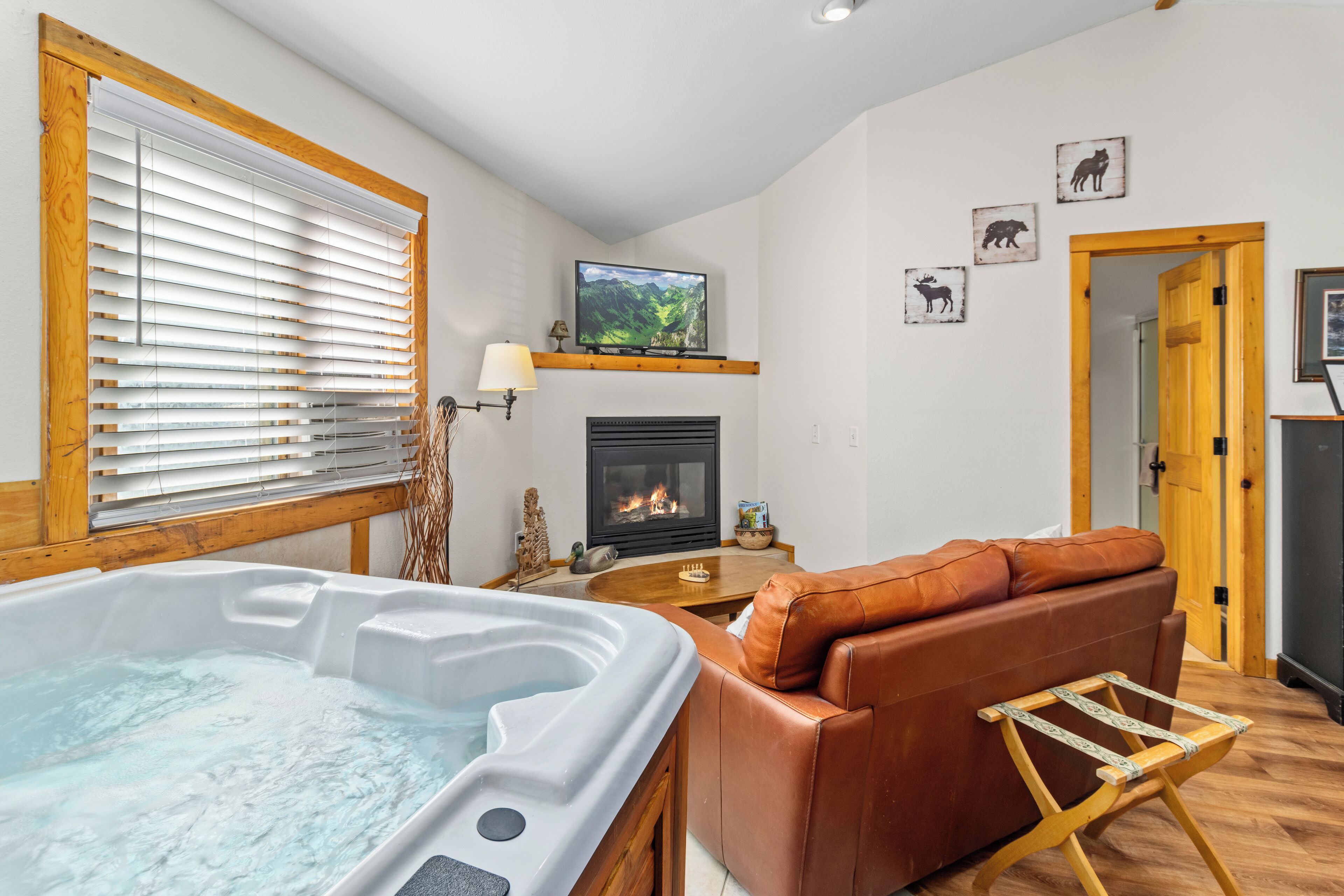 A cozy room with a hot tub, a fireplace, a leather sofa, and a television mounted on the wall.
