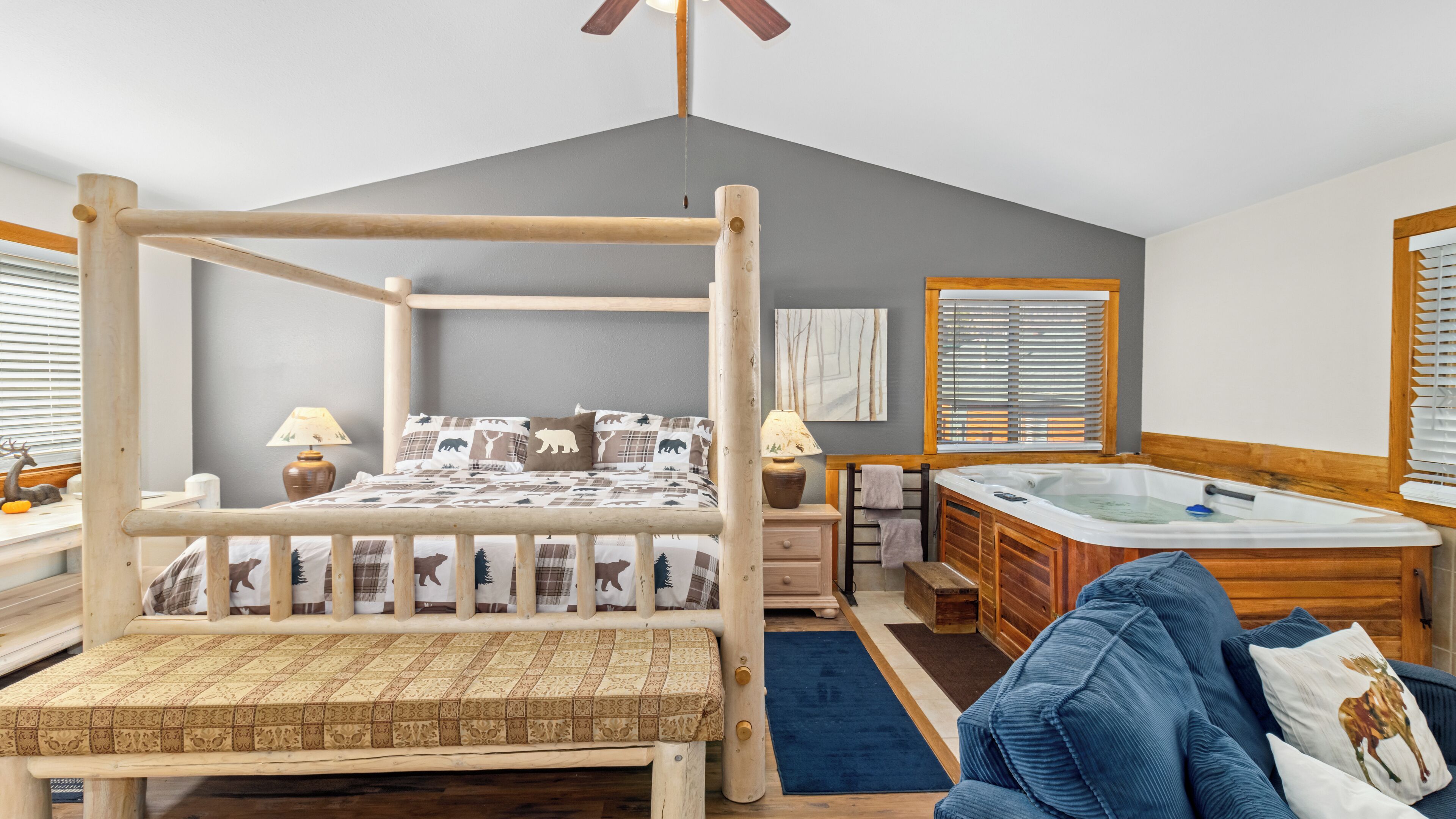 Un dormitorio acogedor de estilo cabaña con una cama con dosel, un banco de madera, un sofá, un tocador de madera, una bañera y una ventana con persianas.