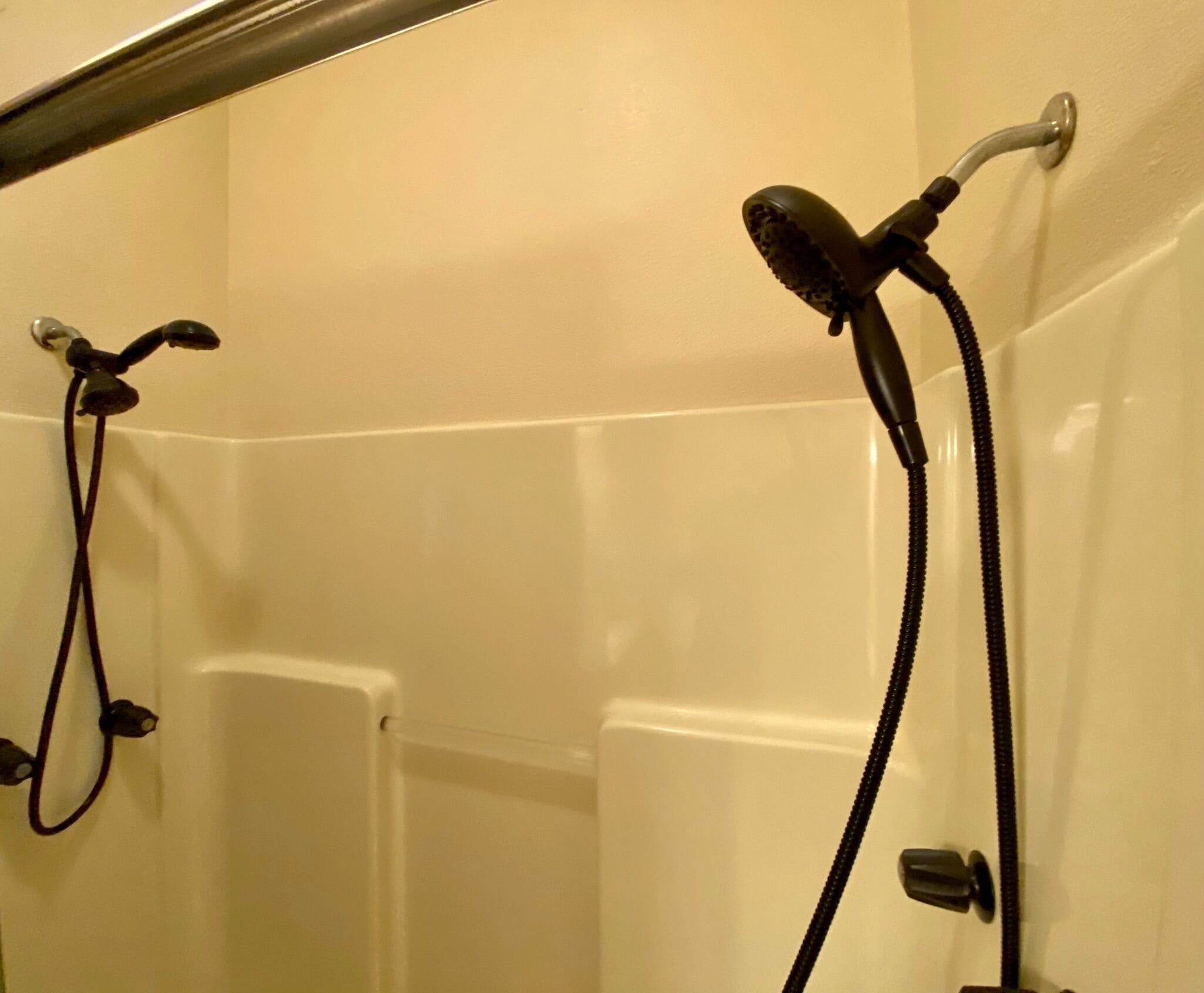 A corner of a bathroom with a bathtub and two showerheads.