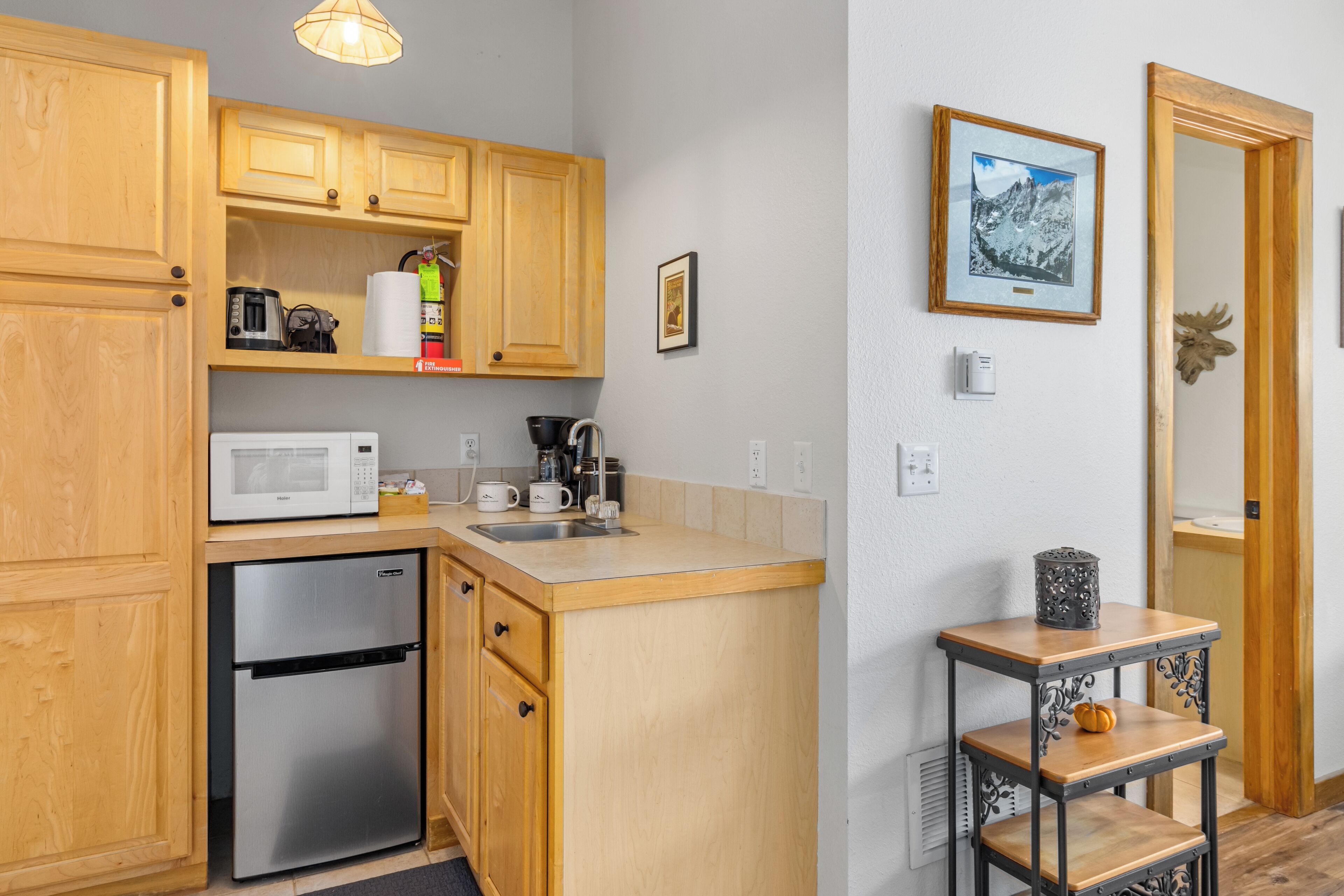 A compact kitchen with wooden cabinets, a microwave, a coffee maker, and a refrigerator.