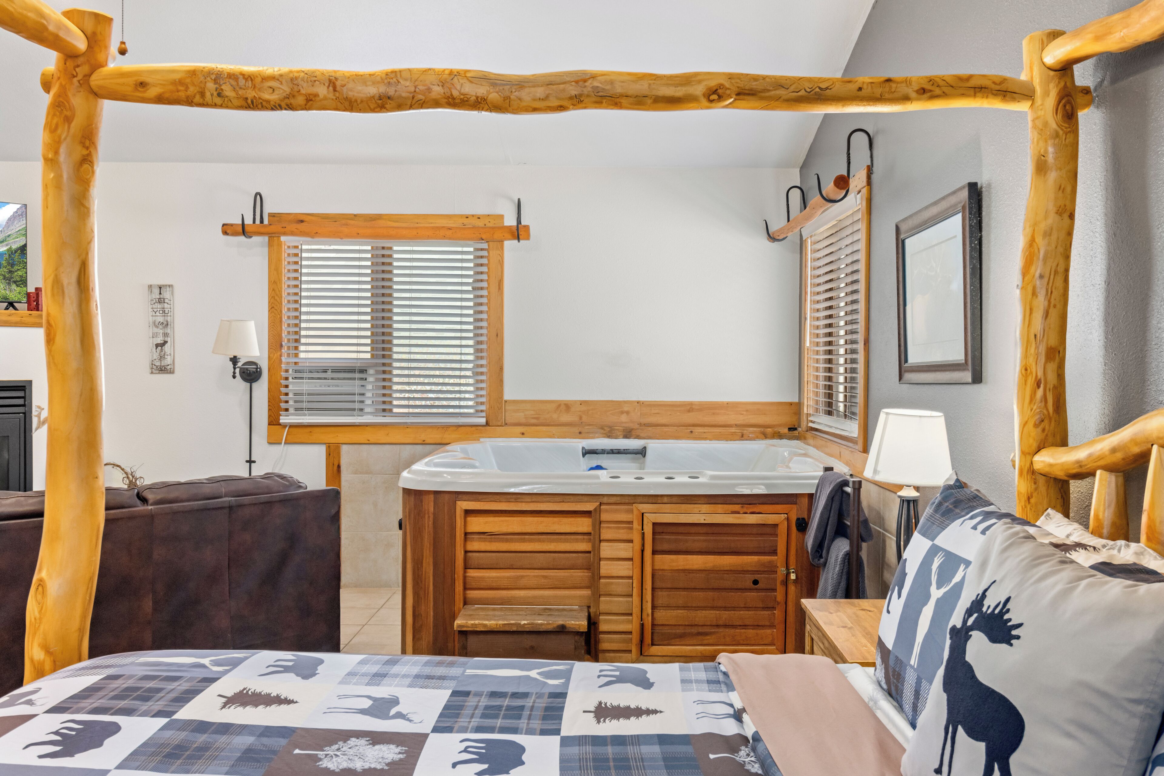 A bedroom with a wooden four-poster bed, a wooden vanity with a sink, and a window with blinds.