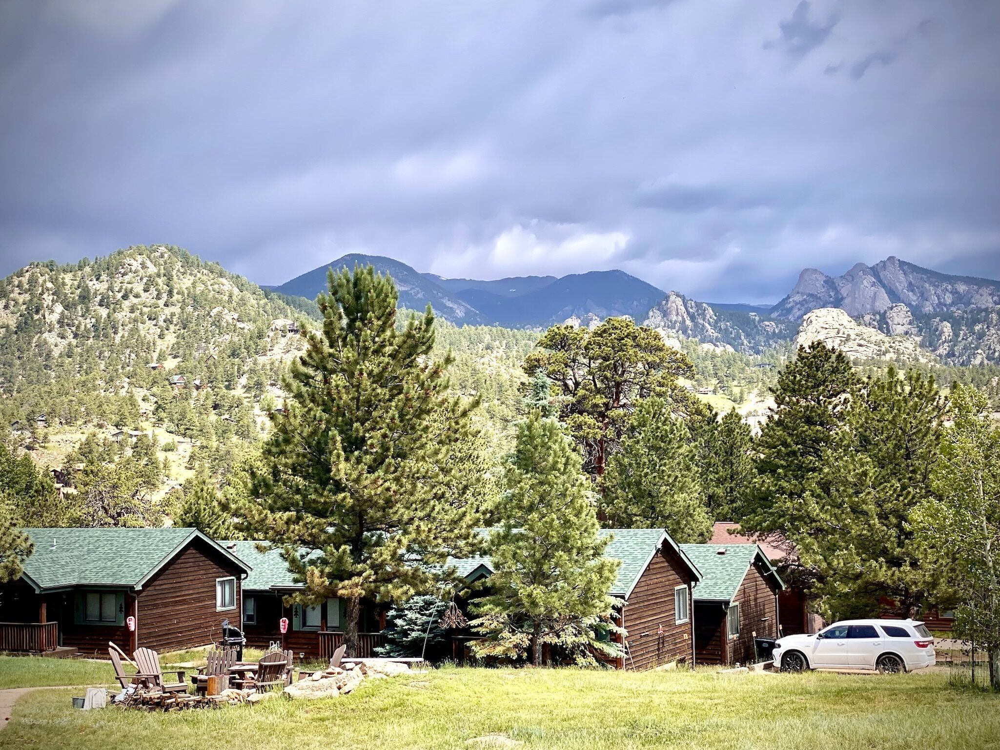 A cabin with a green roof, surrounded by trees and mountains in the background.