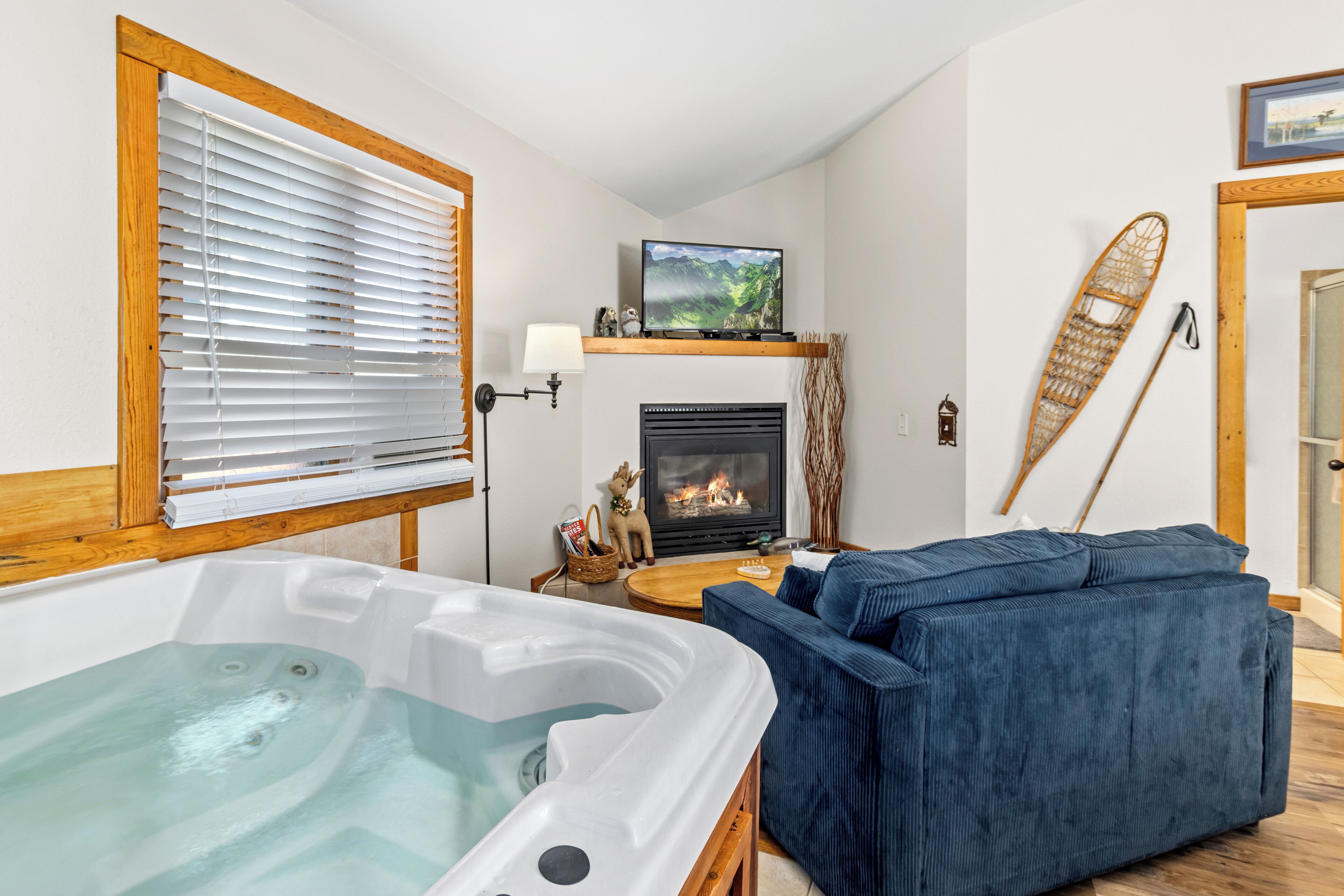 A cozy living room with a fireplace, a large window with blinds, a blue sofa, and a hot tub.