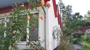 Ein Haus mit weißer Fassade und rotem Zierdekor, umgeben von üppigem Grün und einem gepflegten Garten.
