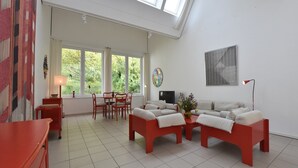 Ein geräumiges Wohnzimmer mit hoher Decke, großen Fenstern, einem Essbereich und einer gemütlichen Sitzecke.