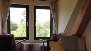 A bedroom with a large window, a bed, two chairs, and a radiator.