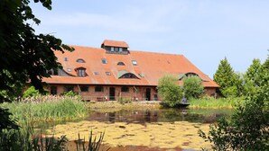 A large brick building with a red-tiled roof, surrounded by a pond and greenery.