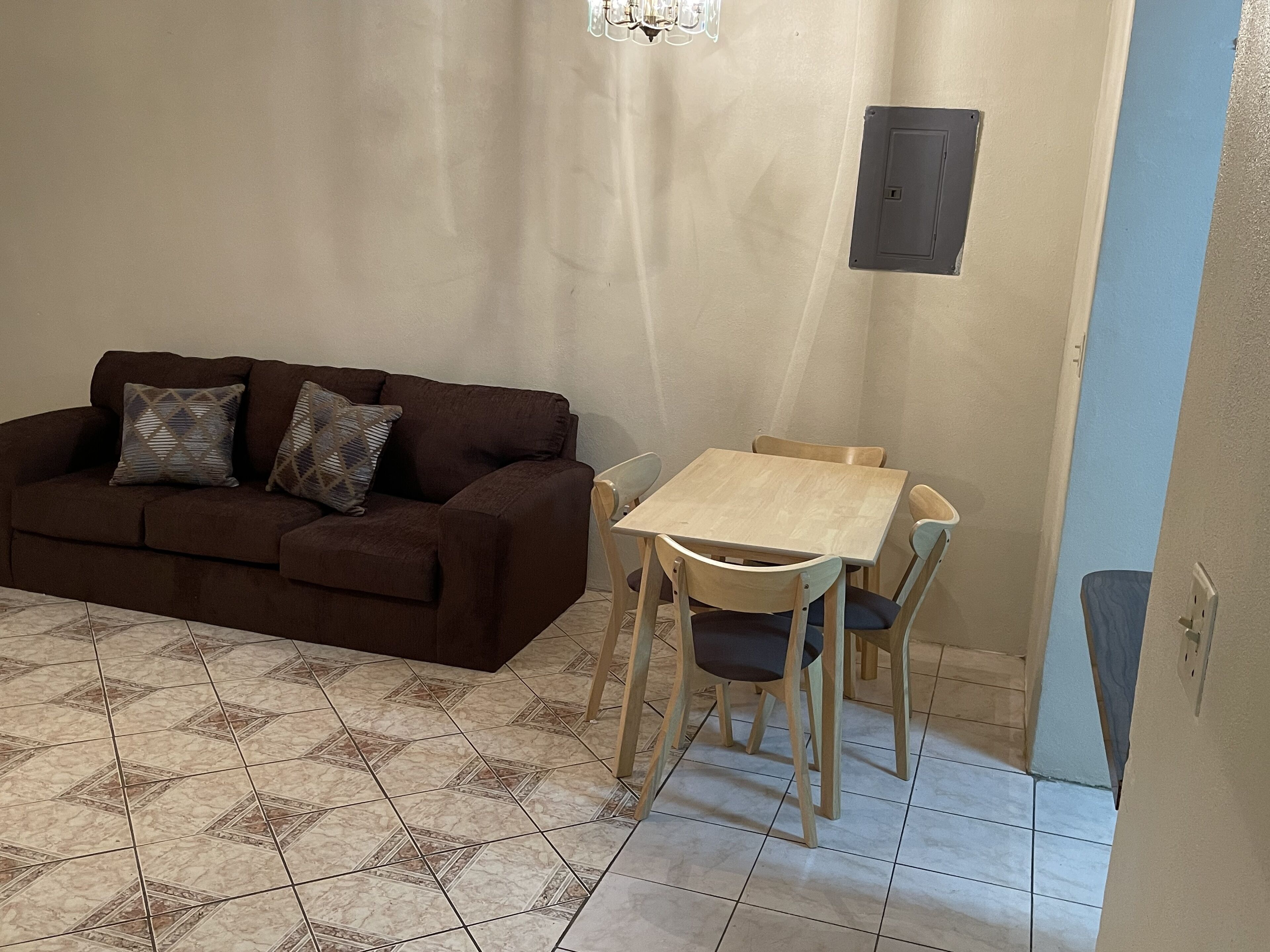 A living room with a brown sofa, patterned cushions, a wooden table, and matching chairs.
