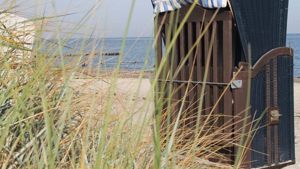 En byggnad vid stranden med en metallgrind, omgiven av högt gräs och med utsikt över havet.