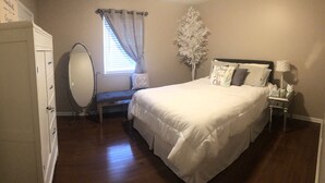 Un dormitorio con cama, cómoda, tocador con espejo, ventana con cortinas y mesita de noche con lámpara.