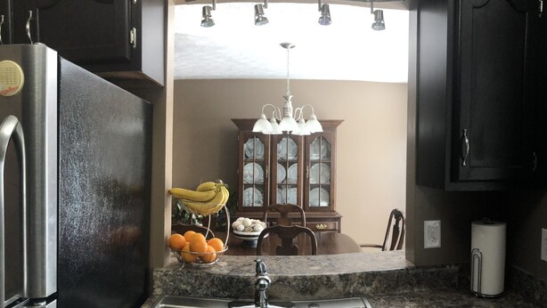 Una cocina con un lavamanos doble, un refrigerador, una mesa de comedor con sillas y una araña.