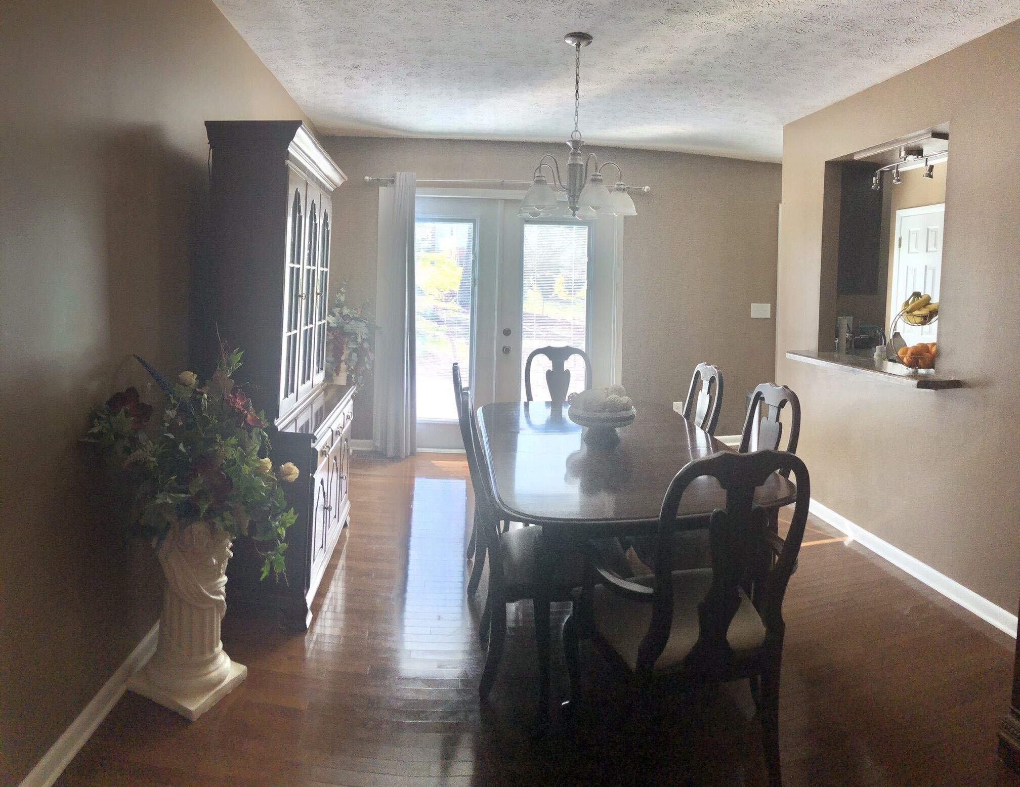 A dining area with a wooden table and chairs, a chandelier, and a potted plant.