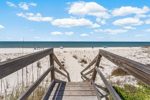 A wooden staircase leading to a sandy beach with a clear sky.